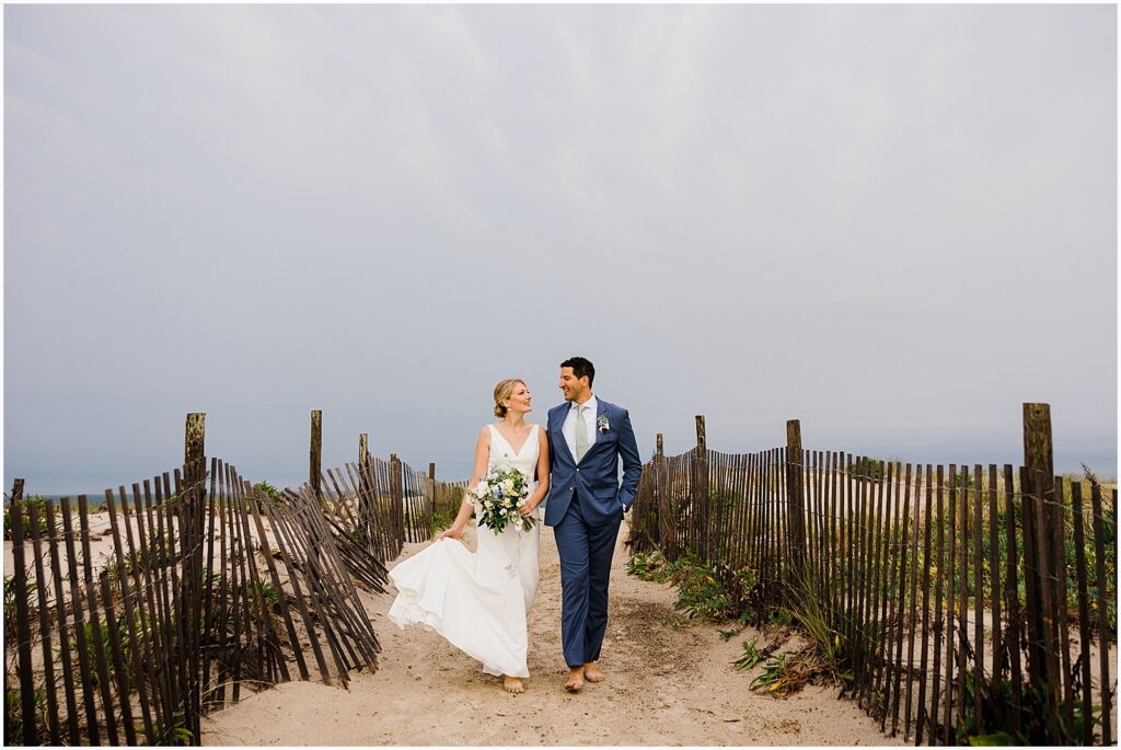 A bride and groom walk over a dune at their Sea Shell Resort wedding.