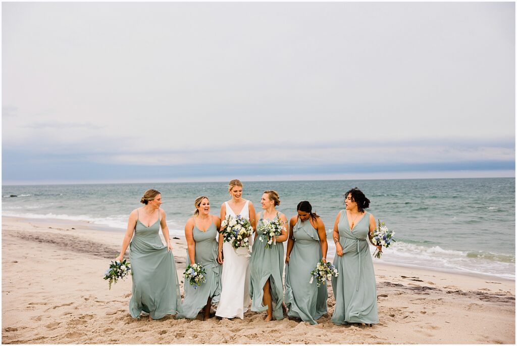 A bride walks down the beach with bridesmaids in green dresses.