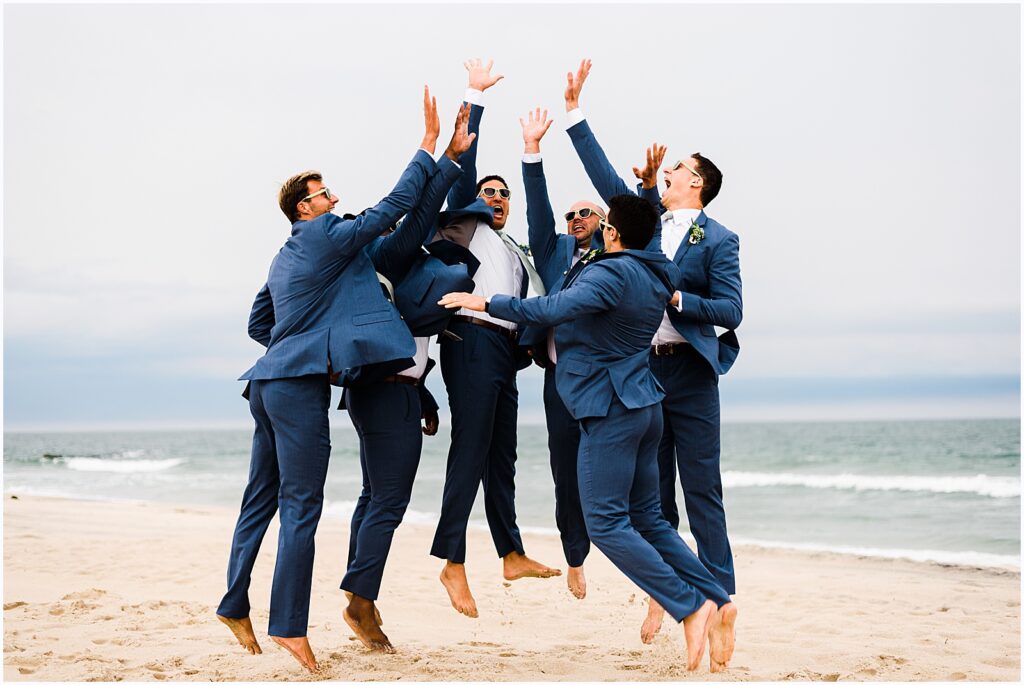 Groomsmen on the beach jump to high five.