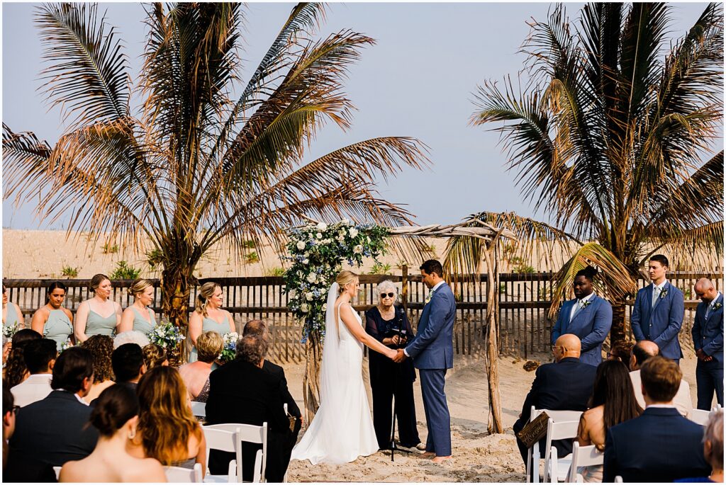 A bride and groom hold hands at the start of a beach wedding ceremony at the Sea Shell Resort.