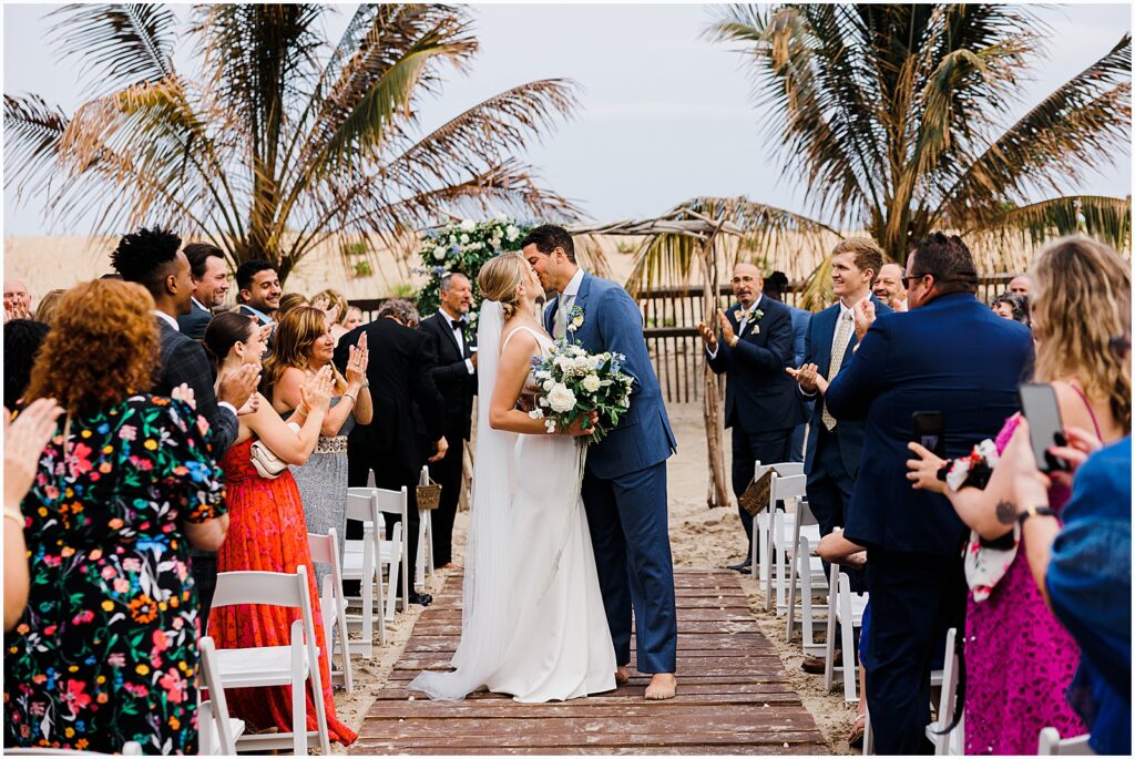 A bride and groom kiss during a wedding recessional on the beach.
