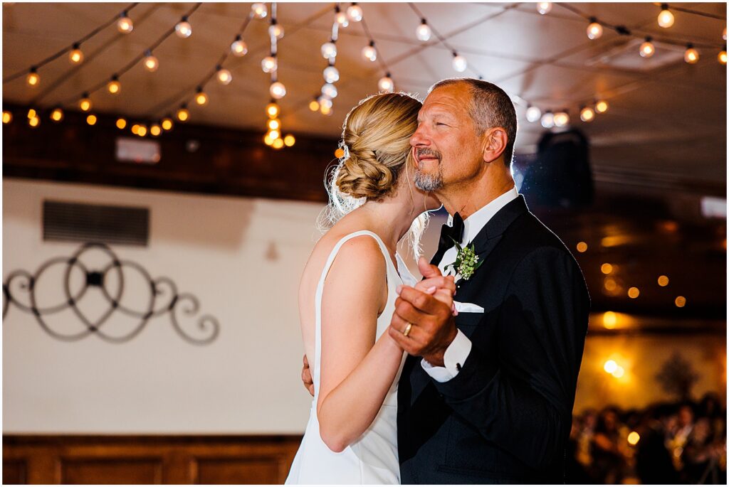 A bride leans on her father during the father daughter dance.