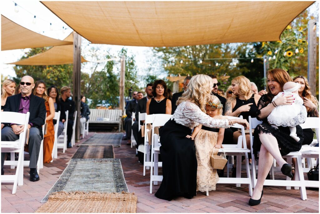 Wedding guests sit in white chairs for a garden wedding ceremony.