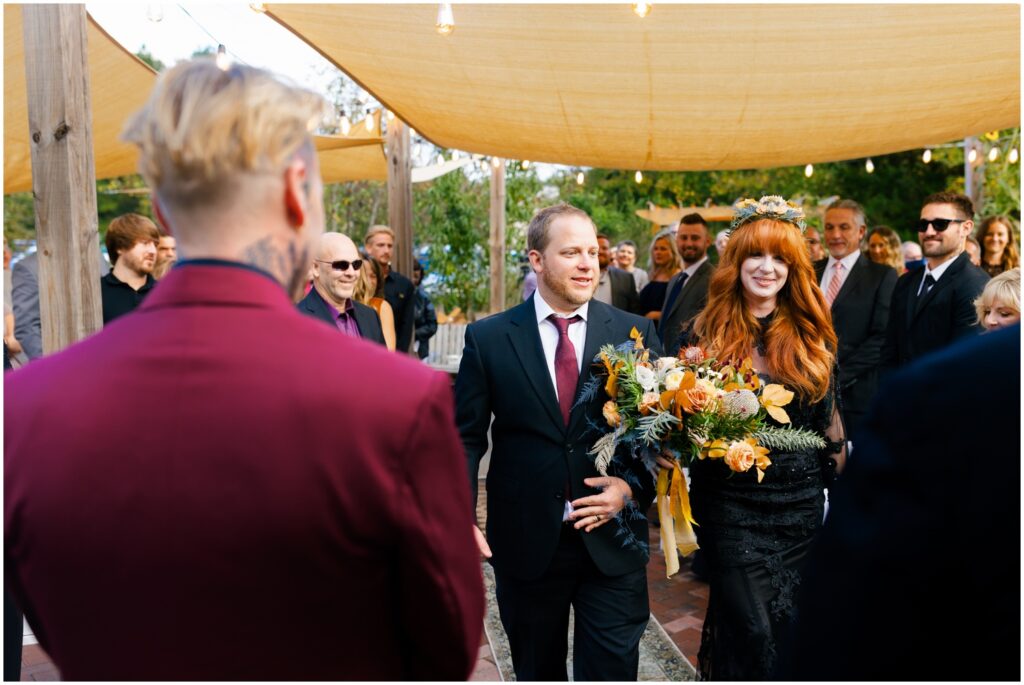 A bride smiles as her father walks her up the aisle at her Good Earth market wedding.