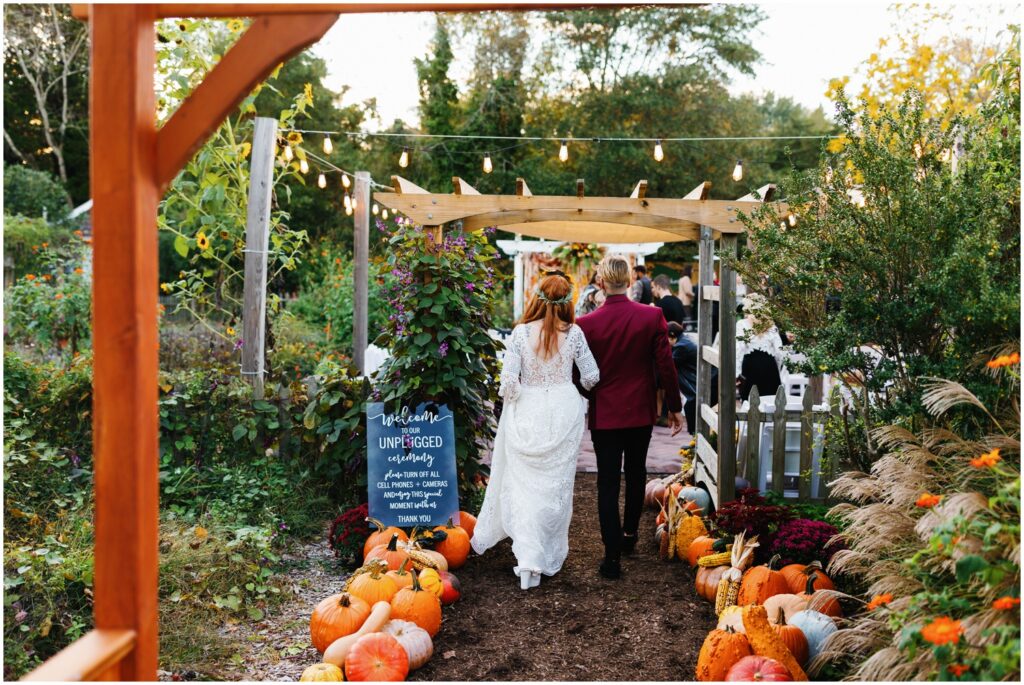 A bride and groom walk between rows of pumpkins to their Good Earth Market wedding reception.
