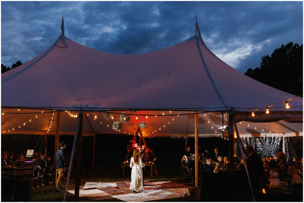 A bride and groom share their first dance under a white reception tent in a field at Good Earth Market.