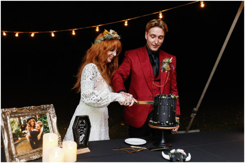 A bride and groom cut a black wedding cake.