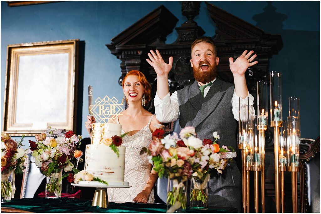 A bride and groom look surprised behind their cake table.
