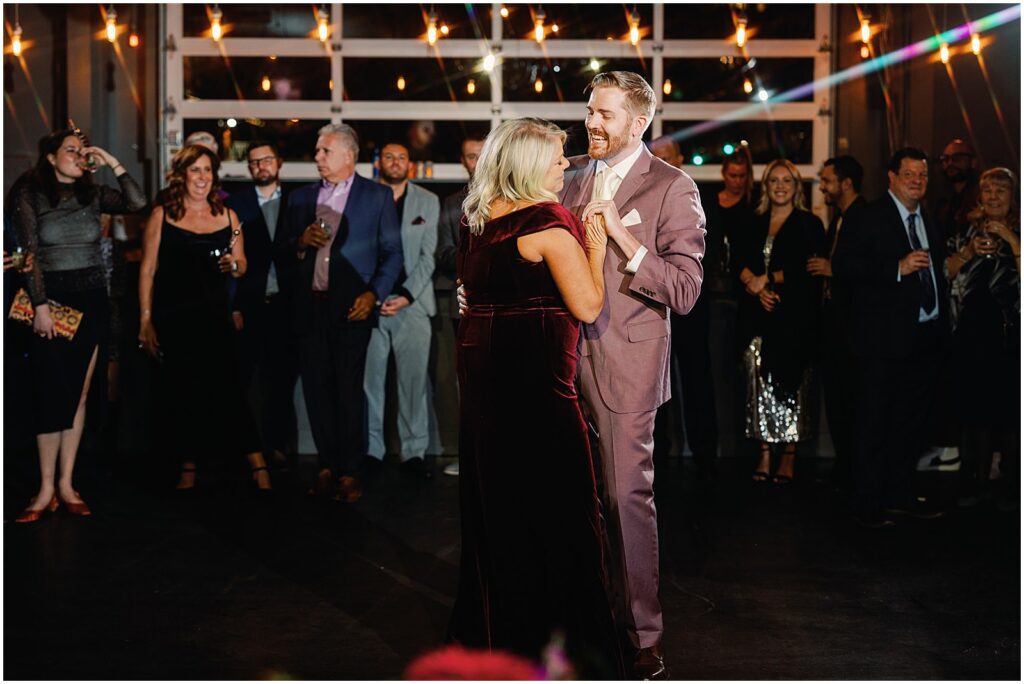 A groom smiles at his mother while he dances with her.