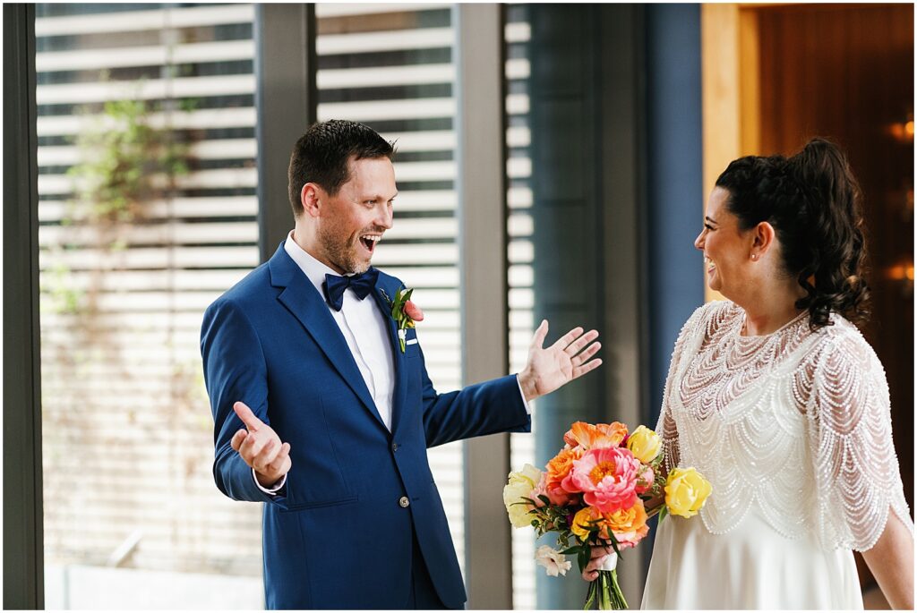 A groom holds out his arms smiling during the first look.