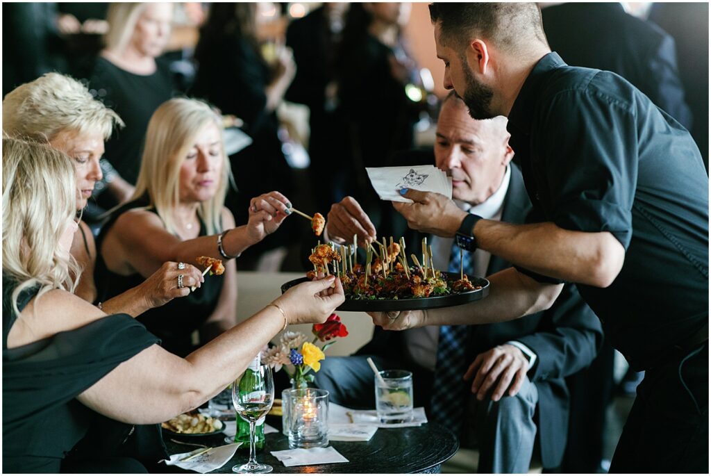 A server lowers a tray of appetizers for guests seated around a table.