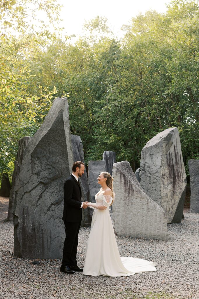 A bride and groom hold hands for a wedding portrait at Grounds for Sculpture's Space of Stone installation.